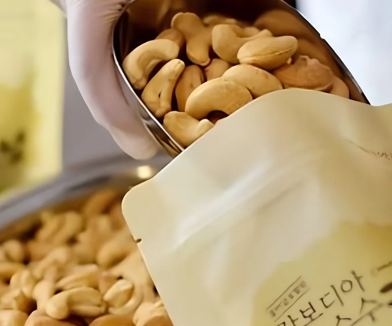 Roasted cashew kernels scooped into a pouch on the Hesed packing line